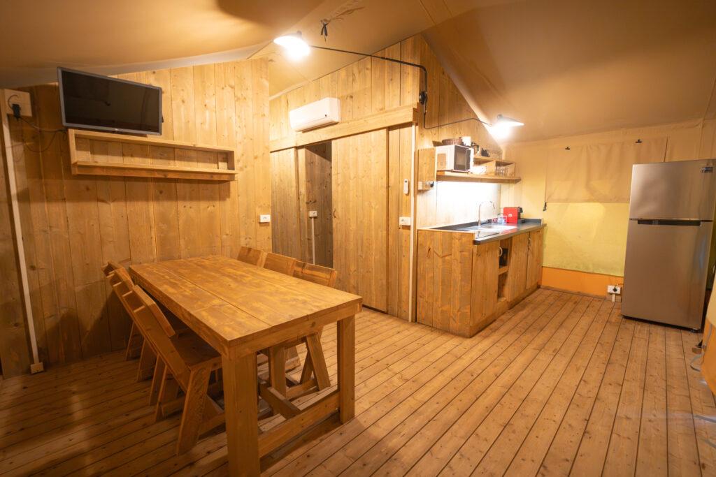 Zona giorno con cucina, tavolo e frigorifero nella Comfort Tent del Camping Village Mediterraneo.