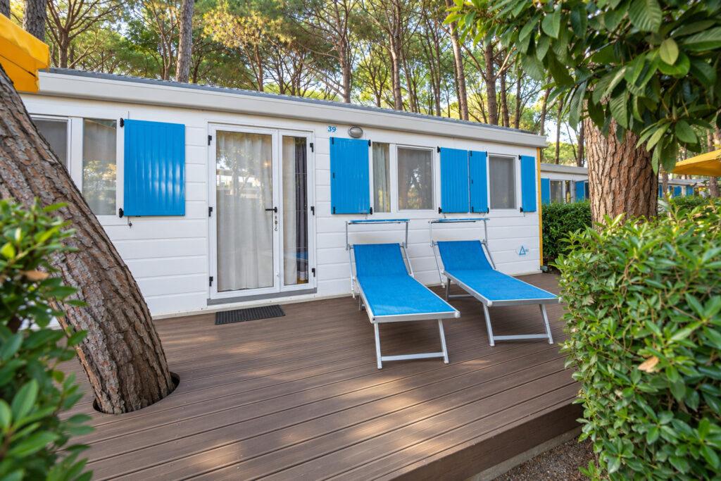 Esterno del Maxi Sole con terrazza in legno e due lettini nel verde del Camping Village Mediterraneo.