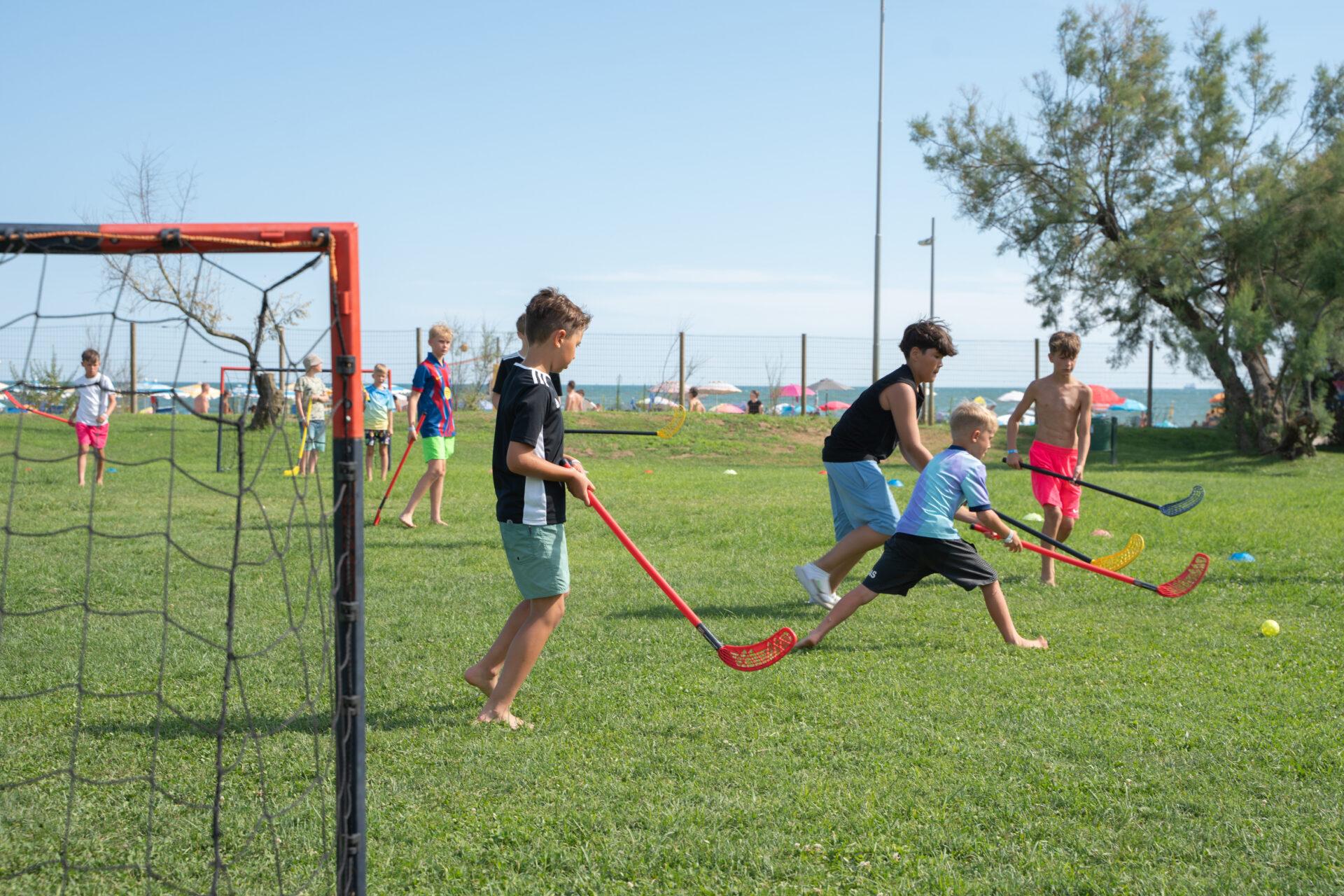Ragazzi giocano a hockey su prato con mazze e pallina nell'area verde del Camping Village Mediterraneo, vicino alla spiaggia