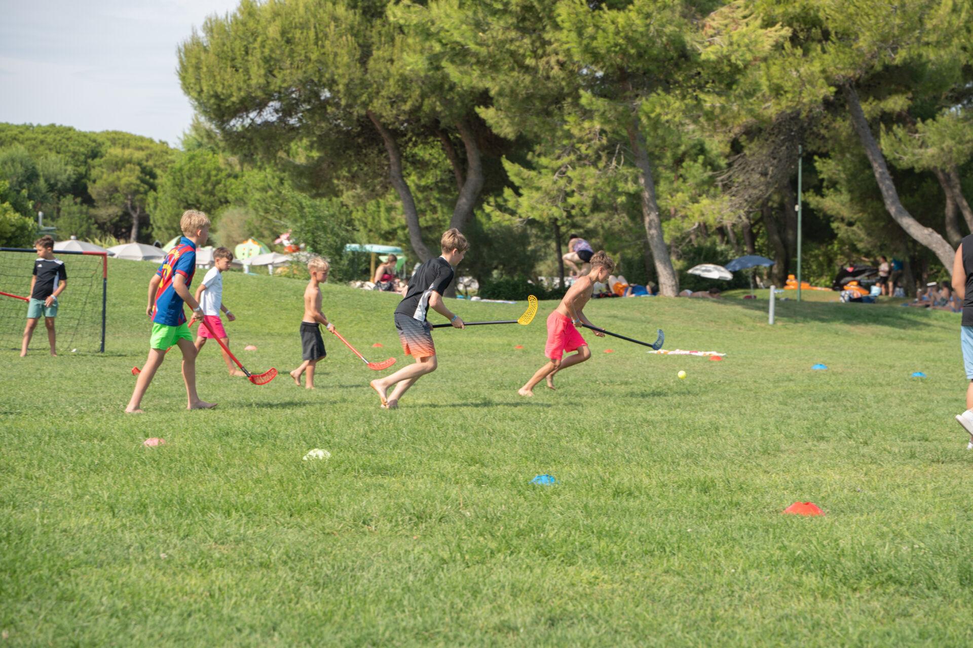 Ragazzi corrono sul prato con mazze da hockey durante una partita all'aperto al Camping Village Mediterraneo