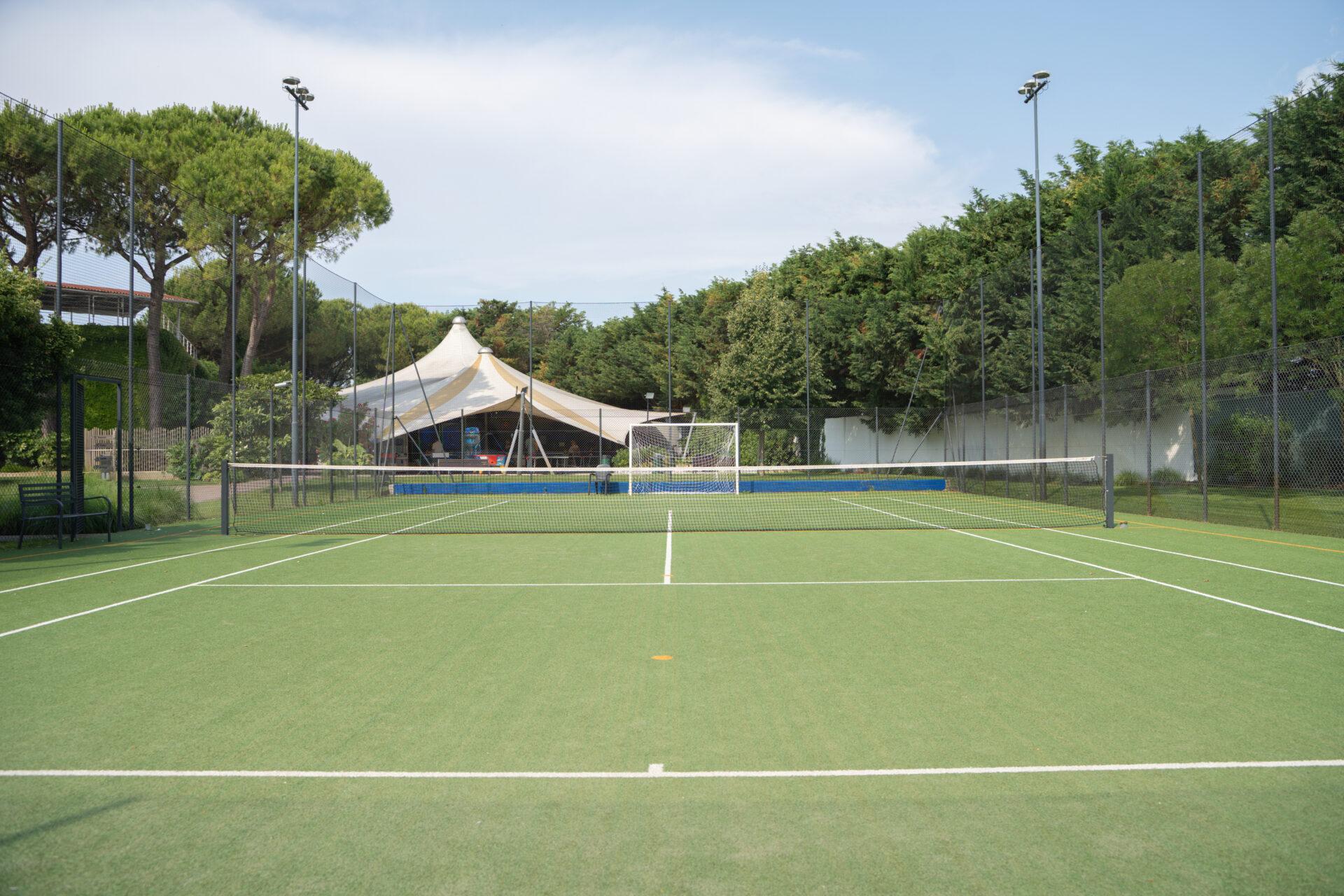 Campo da tennis con rete, recinzione e illuminazione, circondato da alberi al Camping Village Mediterraneo