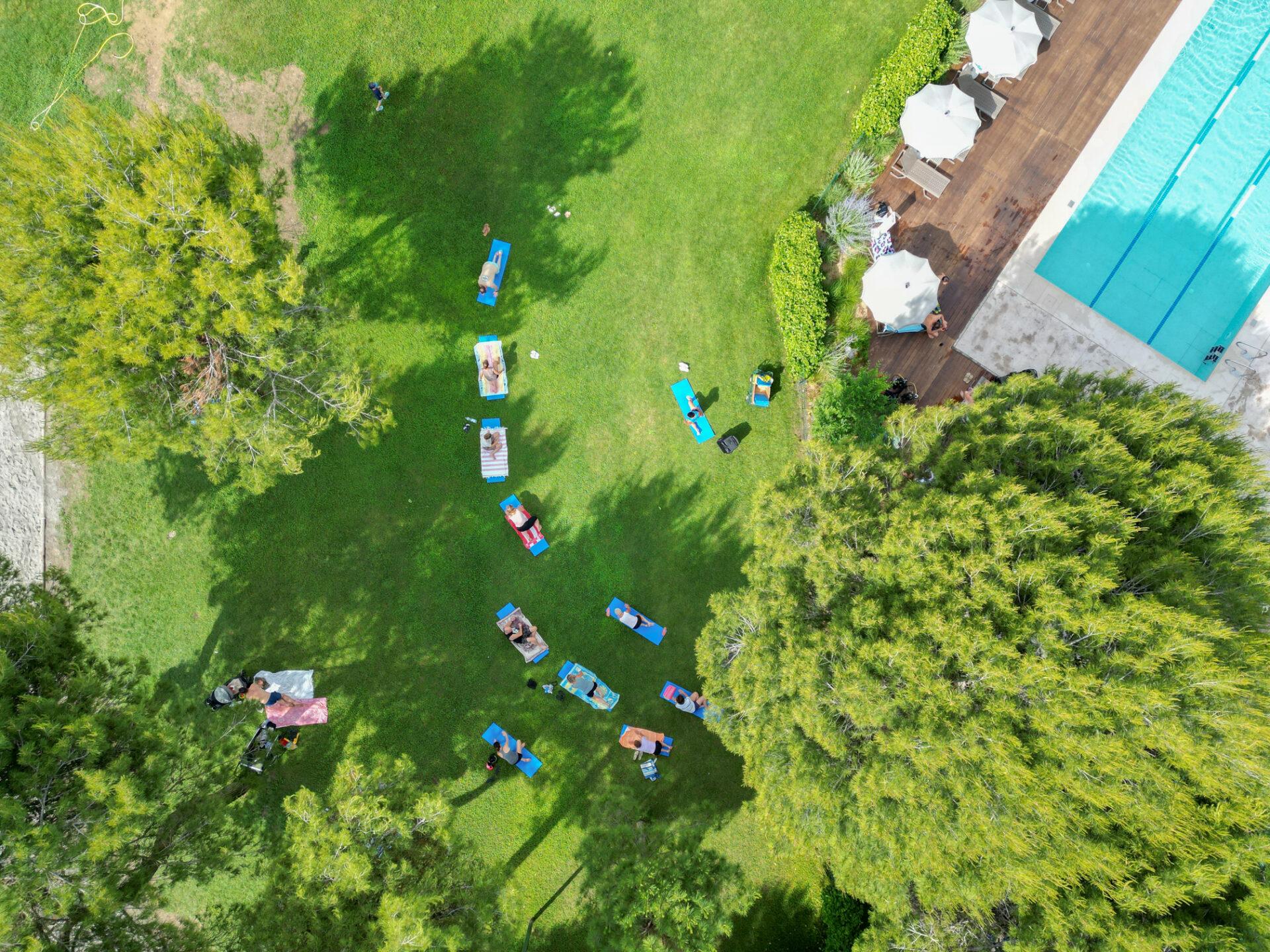 Vista aerea di ospiti distesi sui tappetini durante una sessione di stretching sul prato del Camping Village Mediterraneo
