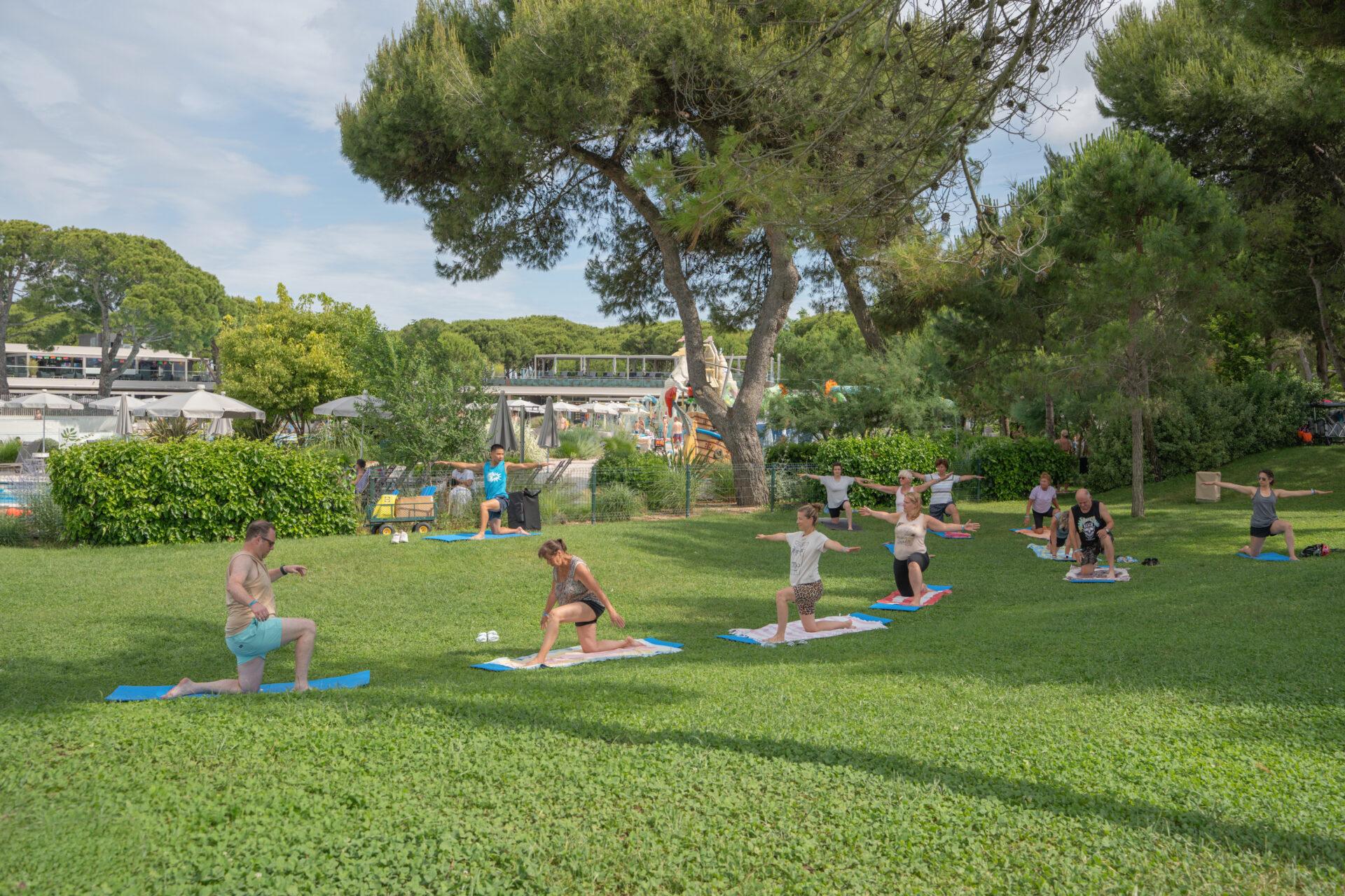 Ospiti eseguono esercizi di stretching sui tappetini in un prato alberato del Camping Village Mediterraneo