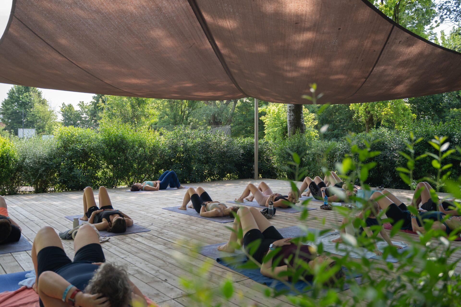 Partecipanti distesi sui tappetini eseguono esercizi di pilates sotto una copertura ombreggiante al Camping Mediterraneo